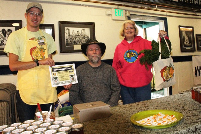 Sitka Farmers Market Assistant Manager Francis Wegman-Lawless, left, and Sitka Farmers Market Manager Debe Brincefield, right, present the Table Of The Day Award to Rock Peterson of Jam-N-Peppers at the fifth Sitka Farmers Market of the 2015 summer on Saturday, Aug. 29, at the Alaska Native Brotherhood Founders Hall in Sitka. Peterson sells an apricot and pepper jam/glaze. He received a gift bag with fresh chard, kale, beets, and other veggies. The market also featured the inaugural Sitka Slug Races, won by Linda Wilson's slug Moses, with Sophie Nethercut and Maybelle Filler's slug Thug The Slug second, and Thomas Witherspoon's slug Slugzilla third. This is the eighth year of Sitka Farmers Markets, hosted by the Sitka Local Foods Network. The last market of the summer is from 10 a.m. to 1 p.m. on Saturday, Sept. 12, at the Alaska Native Brotherhood Founders Hall, 235 Katlian St. For more information about the Sitka Farmers Markets and Sitka Local Foods Network, go to http://www.sitkalocalfoodsnetwork.org/, check out our Facebook page at https://www.facebook.com/SitkaLocalFoodsNetwork, or follow us on Twitter at https://www.twitter.com/SitkaLocalFoods. (PHOTO COURTESY OF SITKA LOCAL FOODS NETWORK)